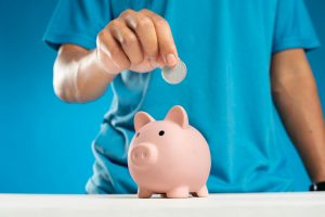 Man smiling, holding money and piggy bank.